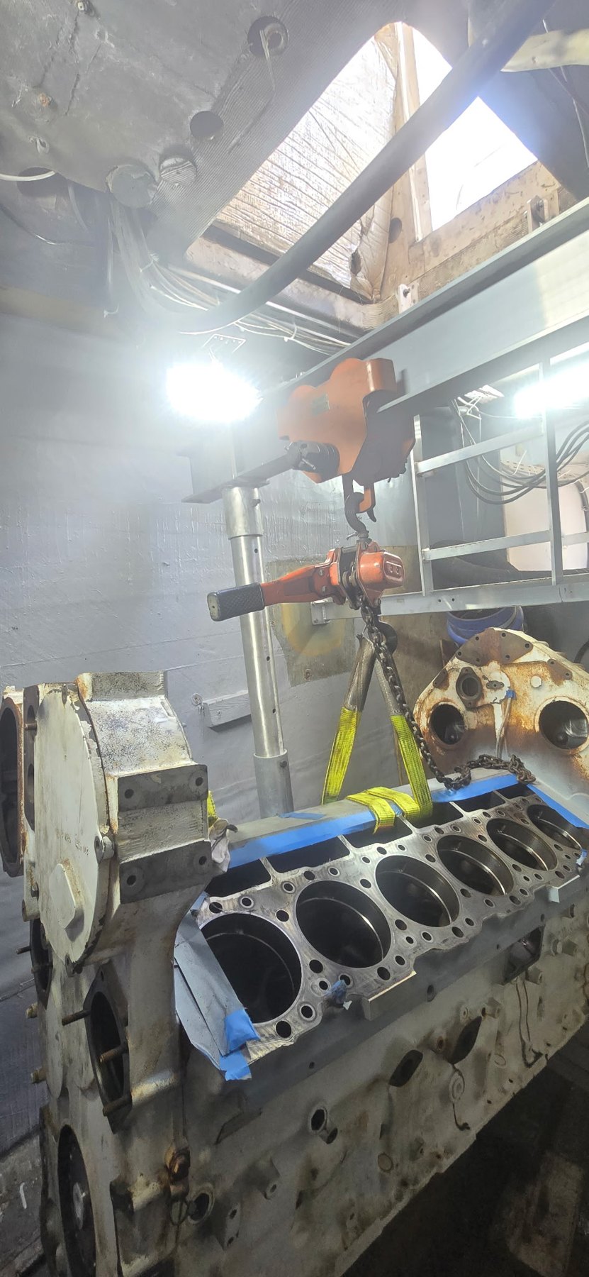 Large V12 marine diesel engine block under chain hoist during overhaul